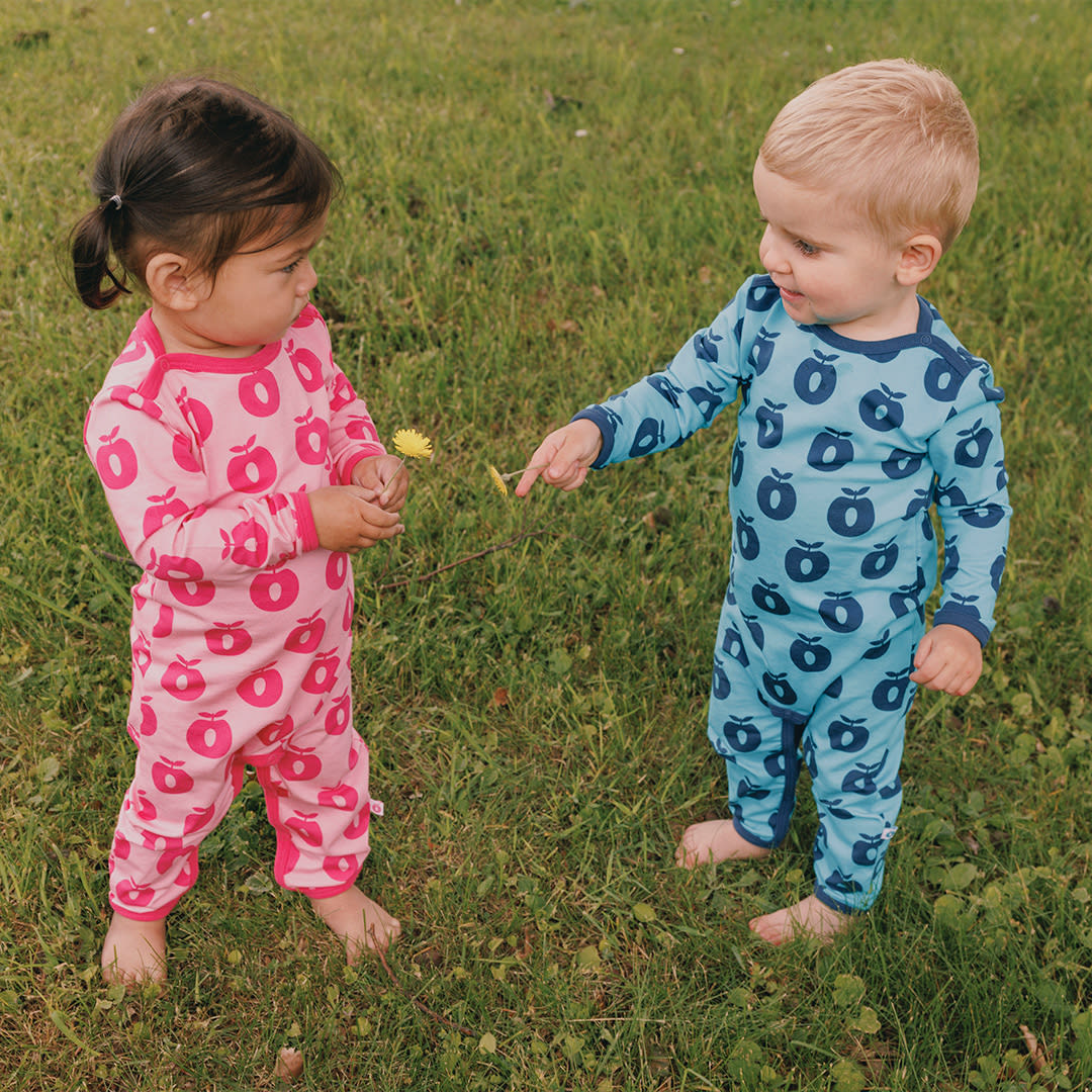 Two children in pajamas standing on grass, one holding a flower.