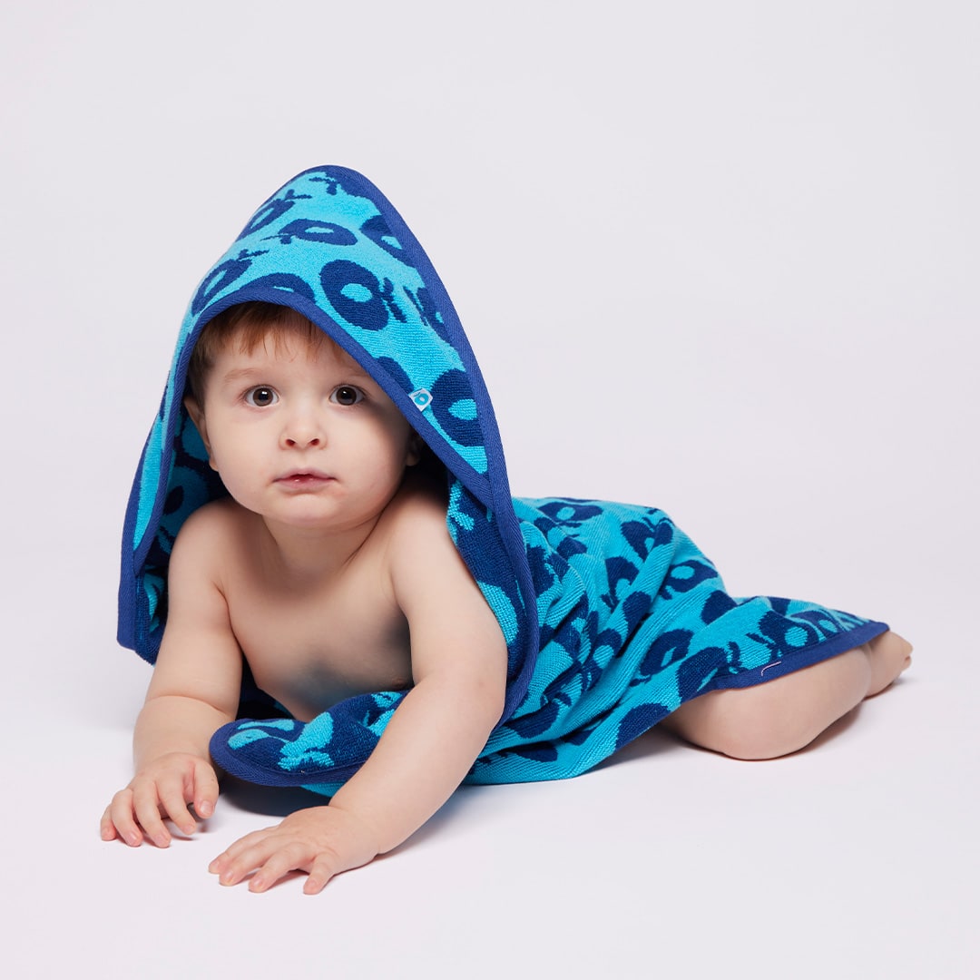 Baby wrapped in a blue hooded towel with a pattern on a light gray background