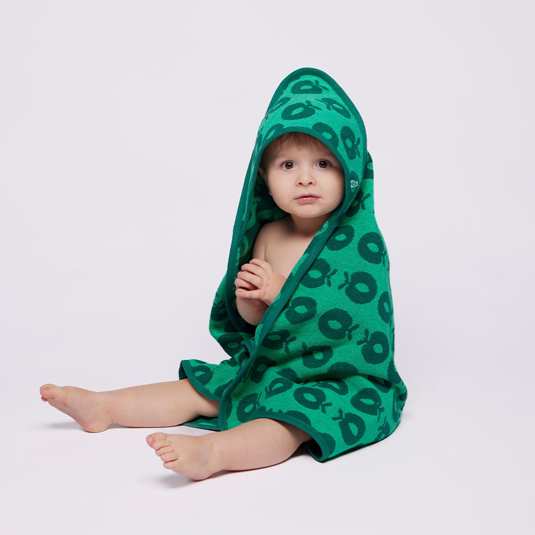 Baby wrapped in a green hooded towel with black patterns on a light gray background