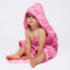 Baby wrapped in a pink hooded towel with a white background